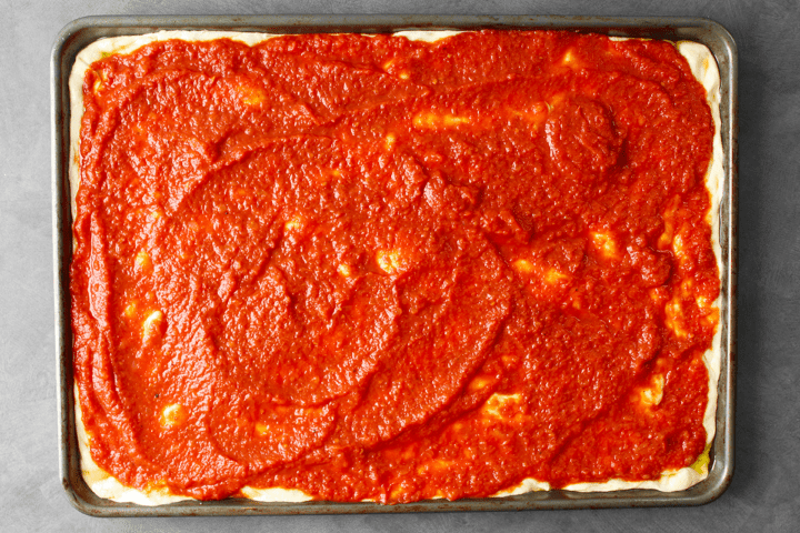 New York style slow-simmered pizza sauce on pizza dough in pan