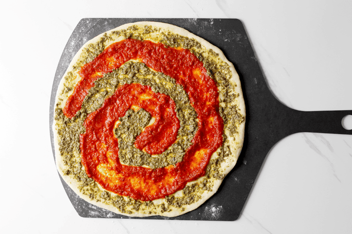 pesto and red sauce on pizza dough